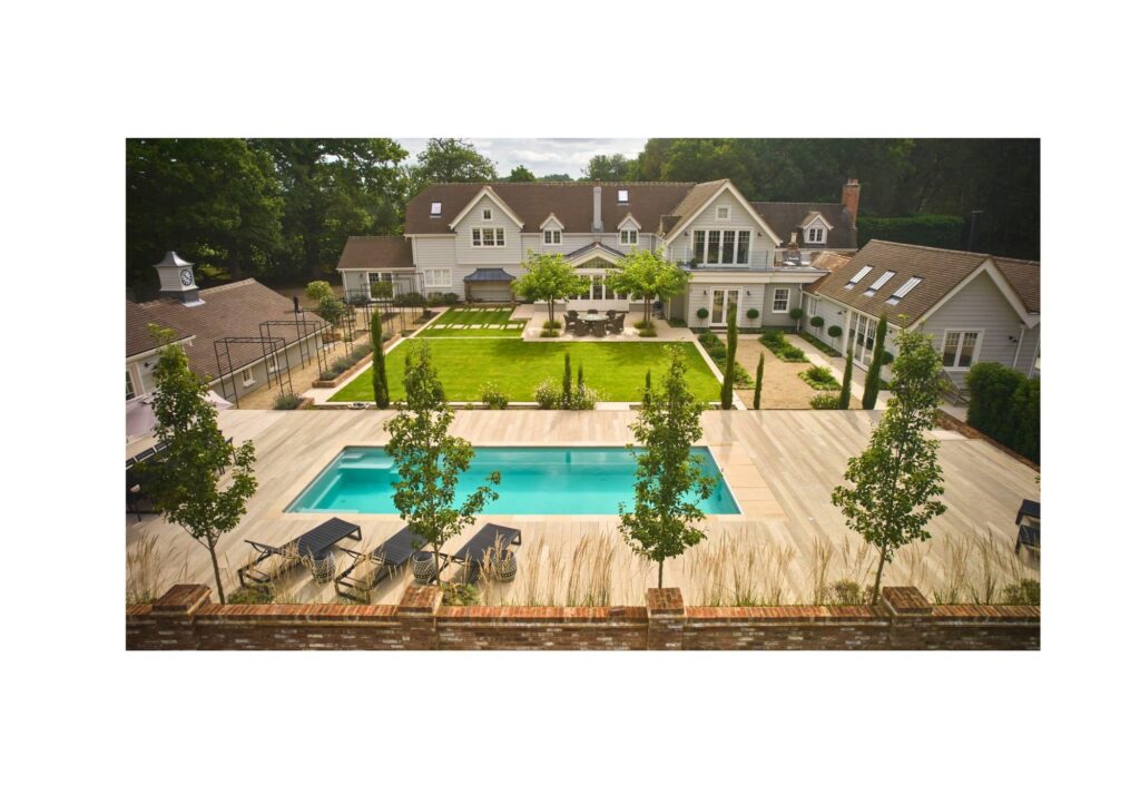 A swimming pool in the back garden surrounded by decking and trees